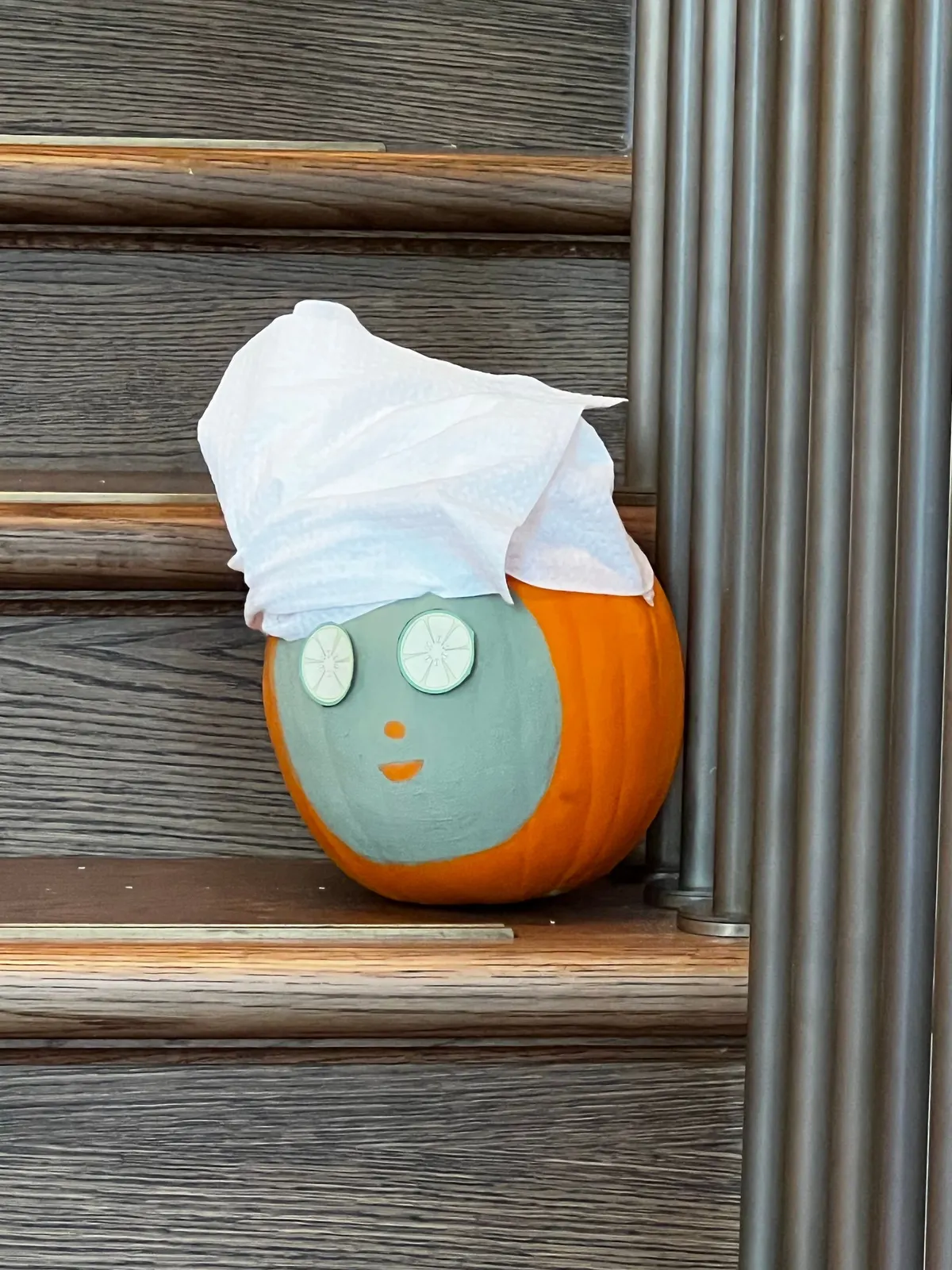 Orange pumpkin painted with a green face mask, paper towel turban and two round green slice eyes