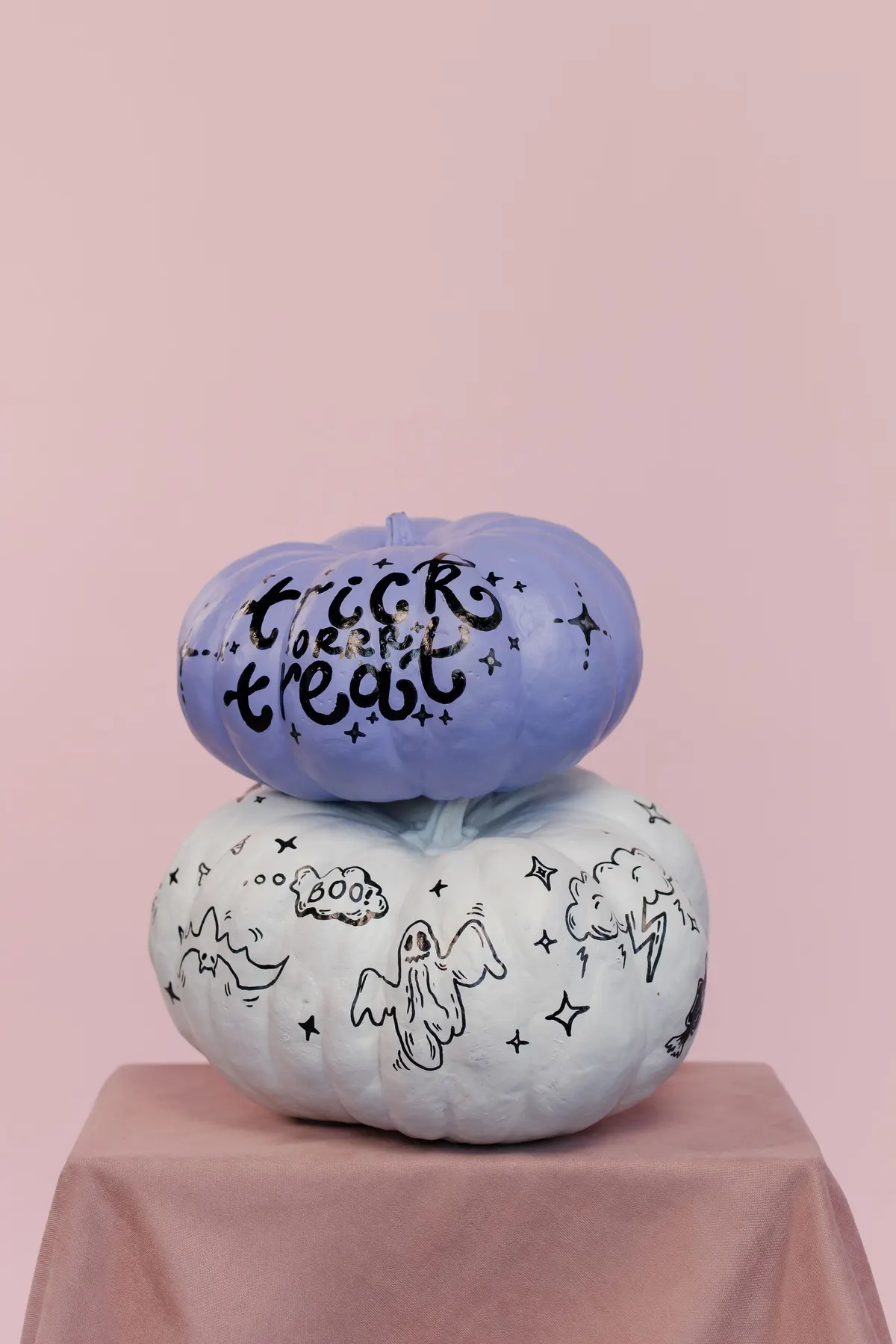 Small lavender pumpkin with black trick or treat lettering and stars stacked on a pale blue-white pumpkin