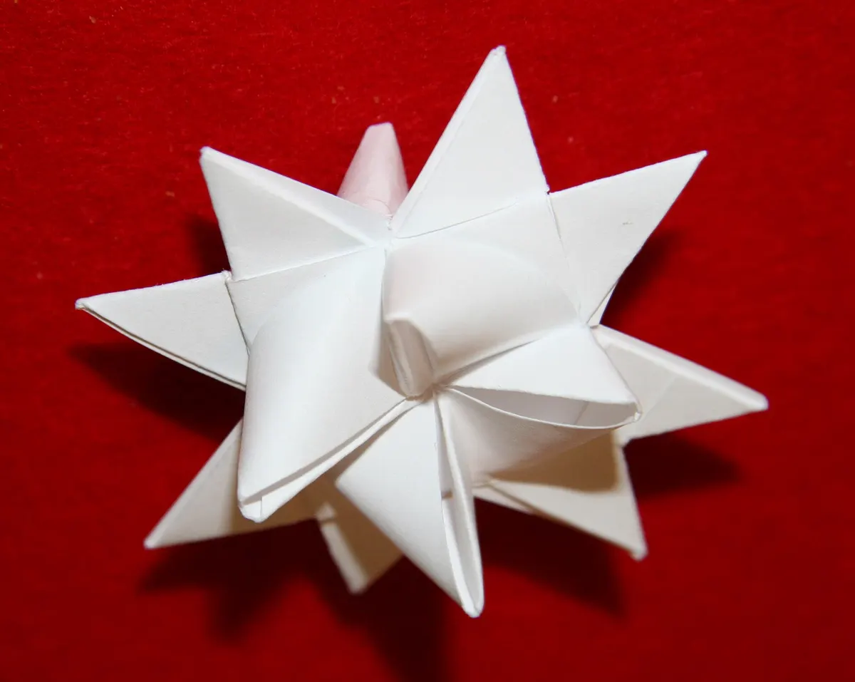 White folded-paper Froebel star with pointed spikes resting on a red fabric background