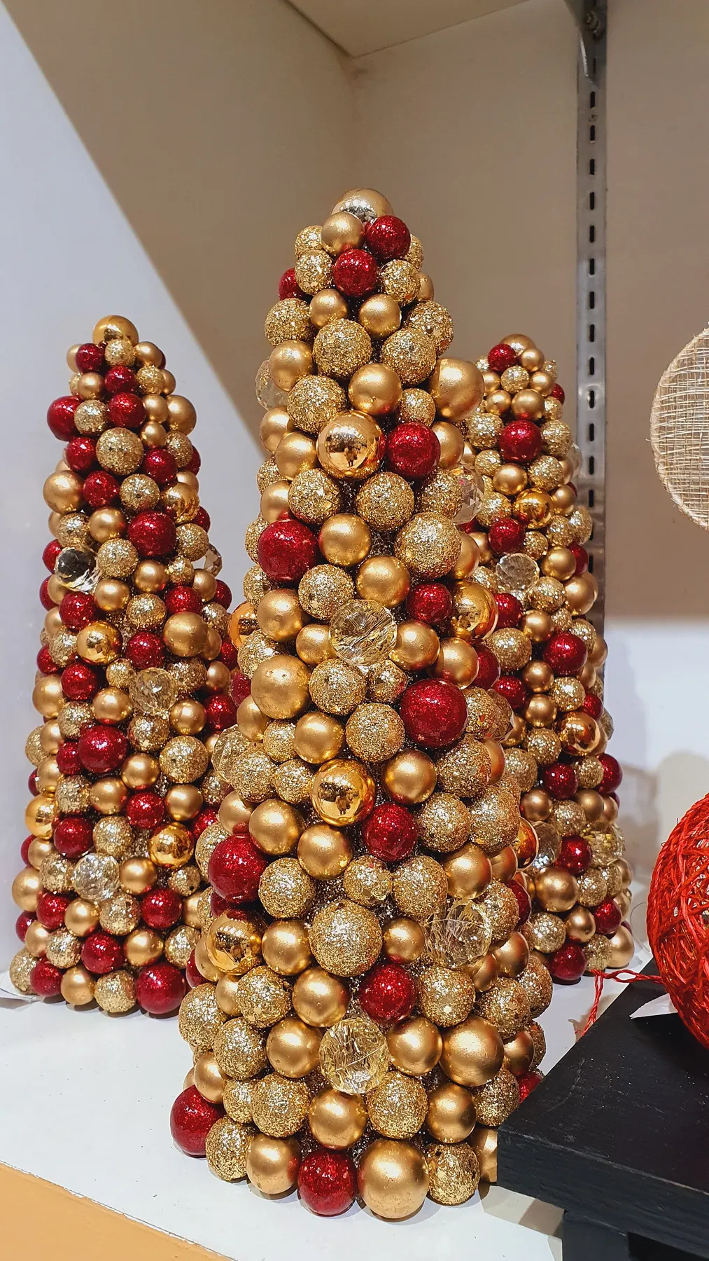 Three cone-shaped tabletop trees built from clustered red and gold baubles on a white shelf