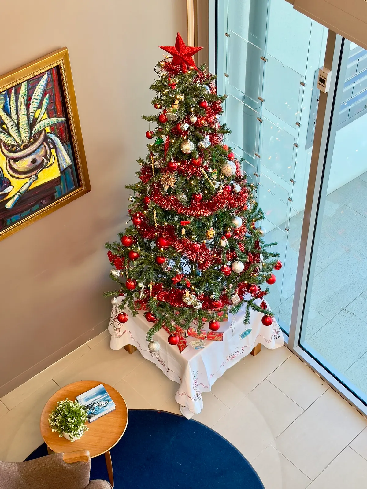 Artificial Christmas tree with red tinsel and star topper raised on a small table draped in white lace