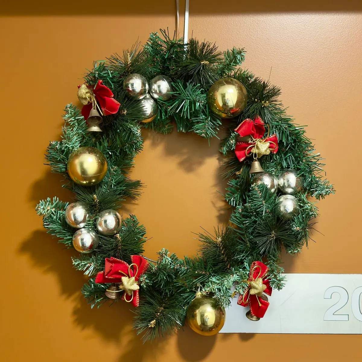 Evergreen wreath with red bows, gold baubles and bells hanging from a ribbon on an apartment door
