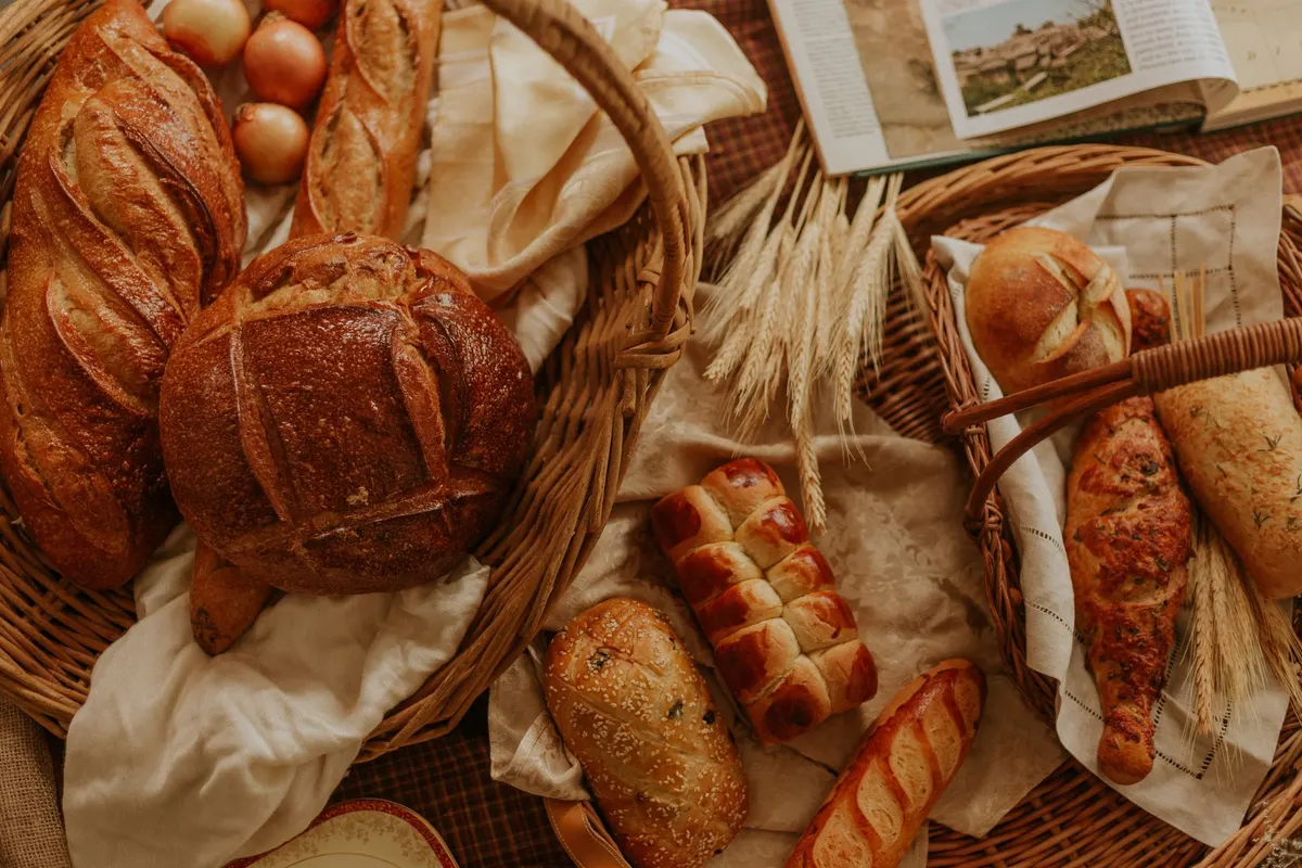 Two wicker baskets of golden-brown bread with onions, wheat bundles and cream linens on a plaid surface