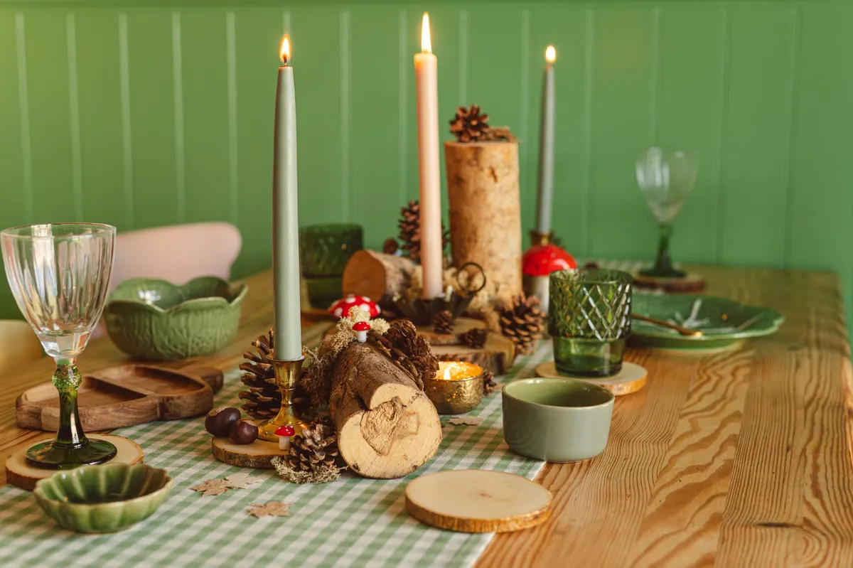 Green gingham table runner with three lit taper candles, logs, wood slices, pinecones and red and white mushroom ornaments