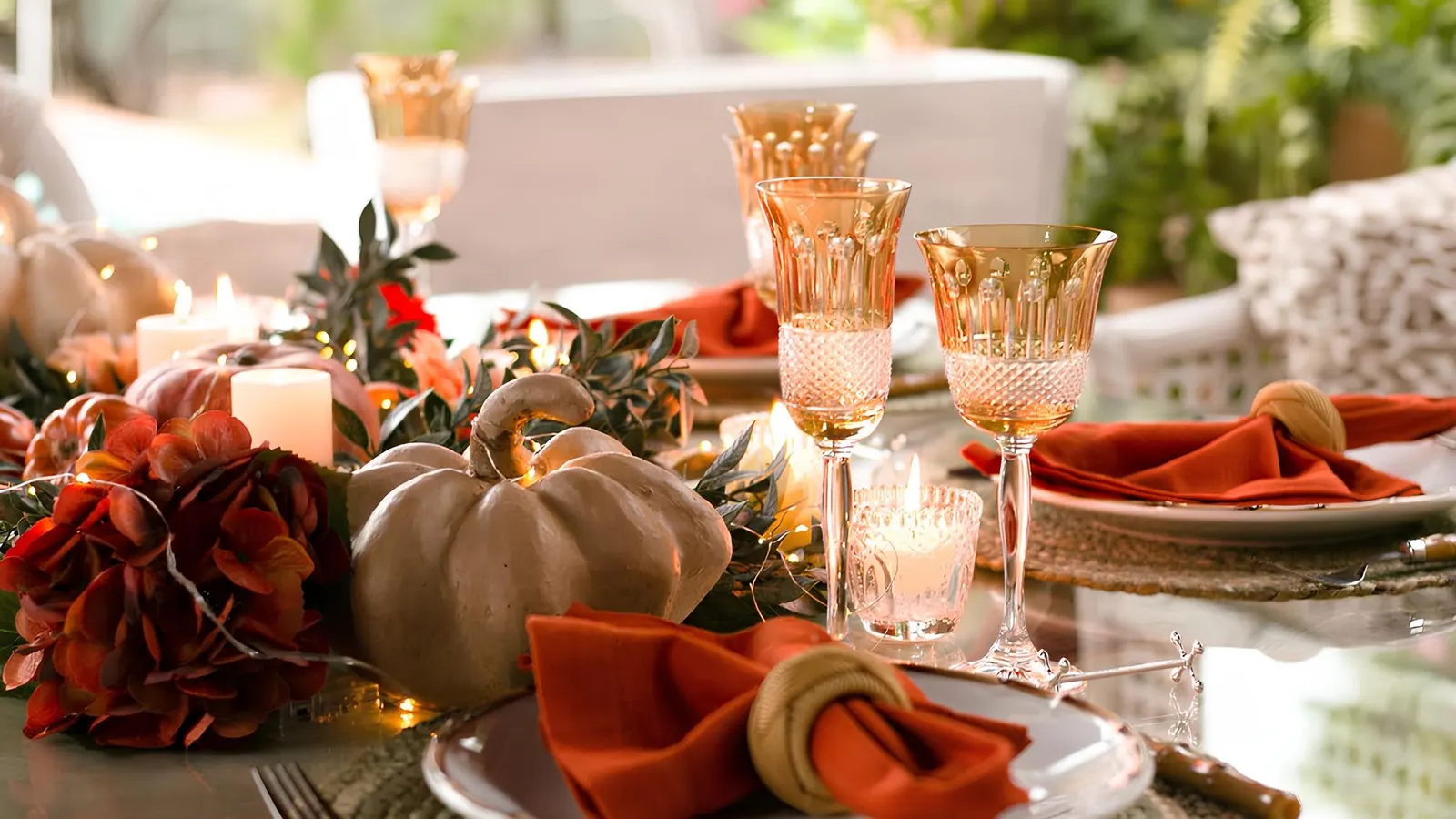 Glass-top table with a low pumpkin and hydrangea centerpiece, lit candles, amber goblets and rust napkins in rattan rings