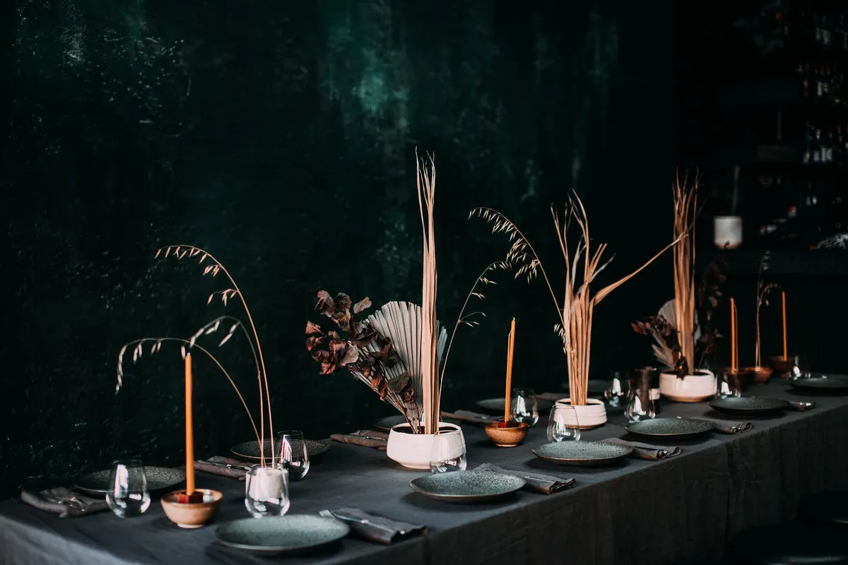 Long table with charcoal linen, grey ceramic plates, orange taper candles in terracotta holders and dried pampas in white pots