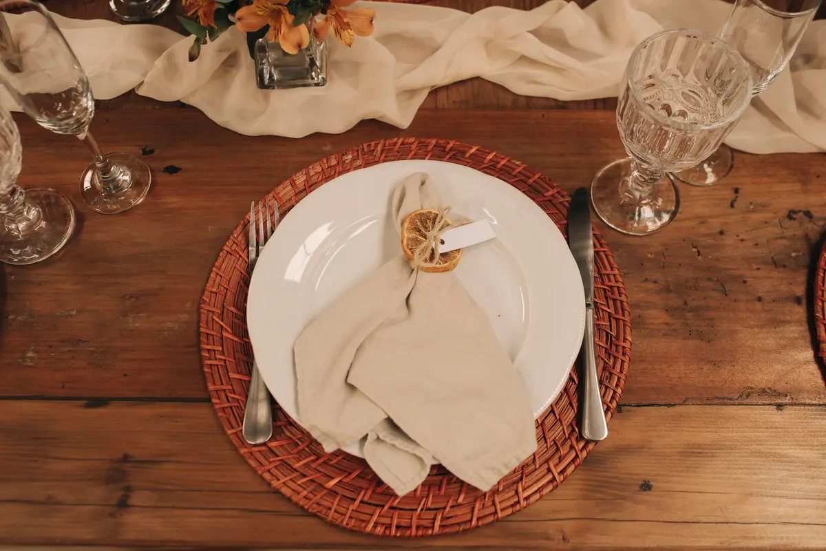 Overhead place setting with rattan charger, white plate and linen napkin tied with twine and a dried orange slice