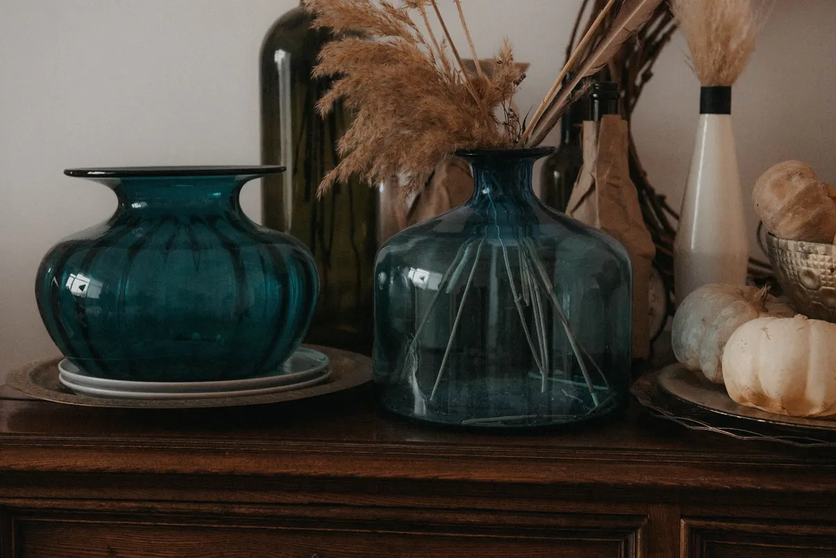 Dark wood sideboard with teal glass vases, dried pampas grass in a blue jug and white pumpkins in a bowl