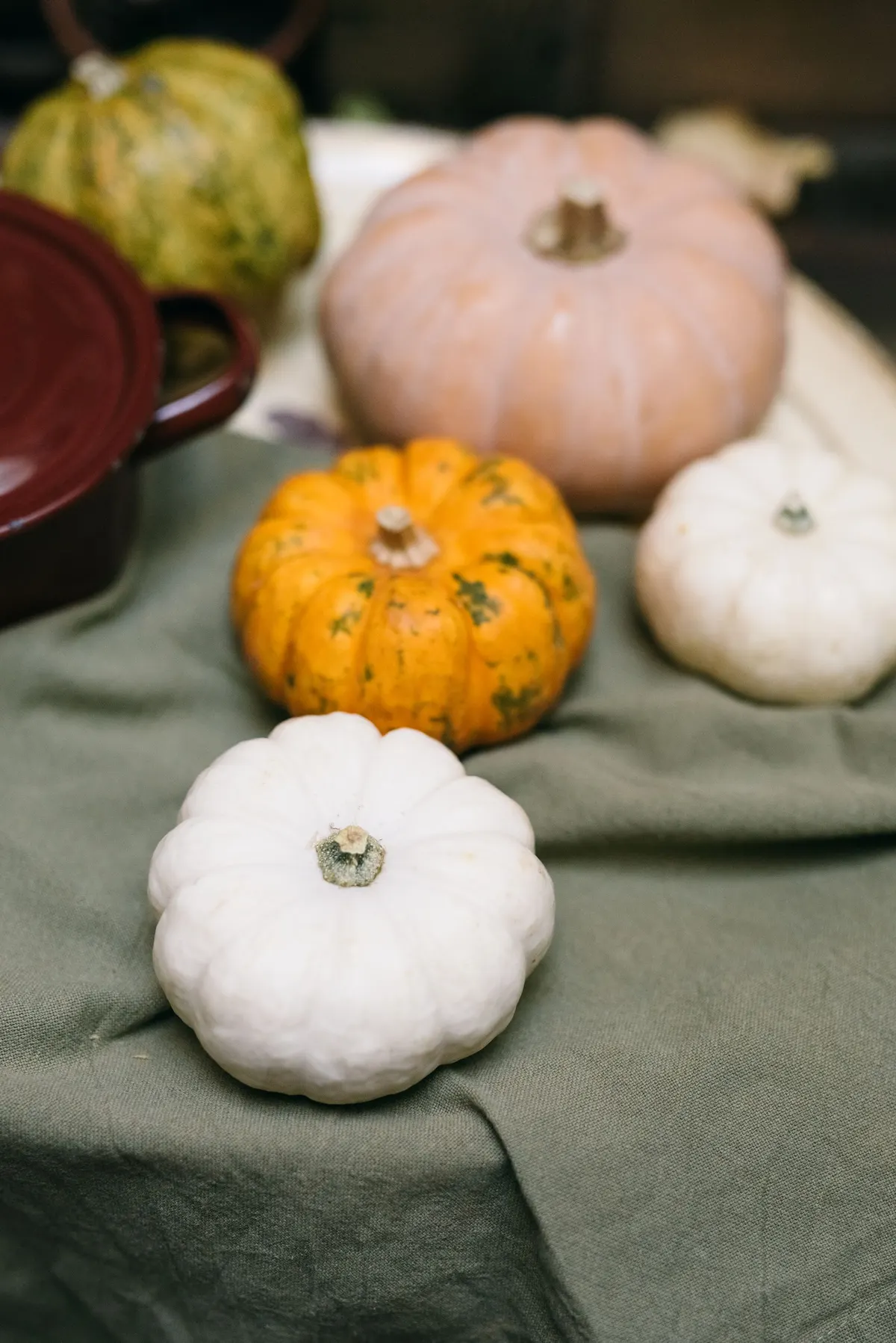 White, pale pink and orange pumpkins of different sizes grouped on wrinkled sage green linen