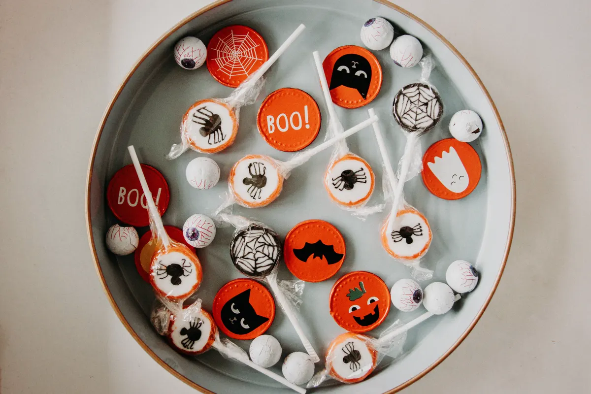 Shallow oval tray of Halloween candy: spider and web lollipops in clear wrappers, foil ghost and bat coins