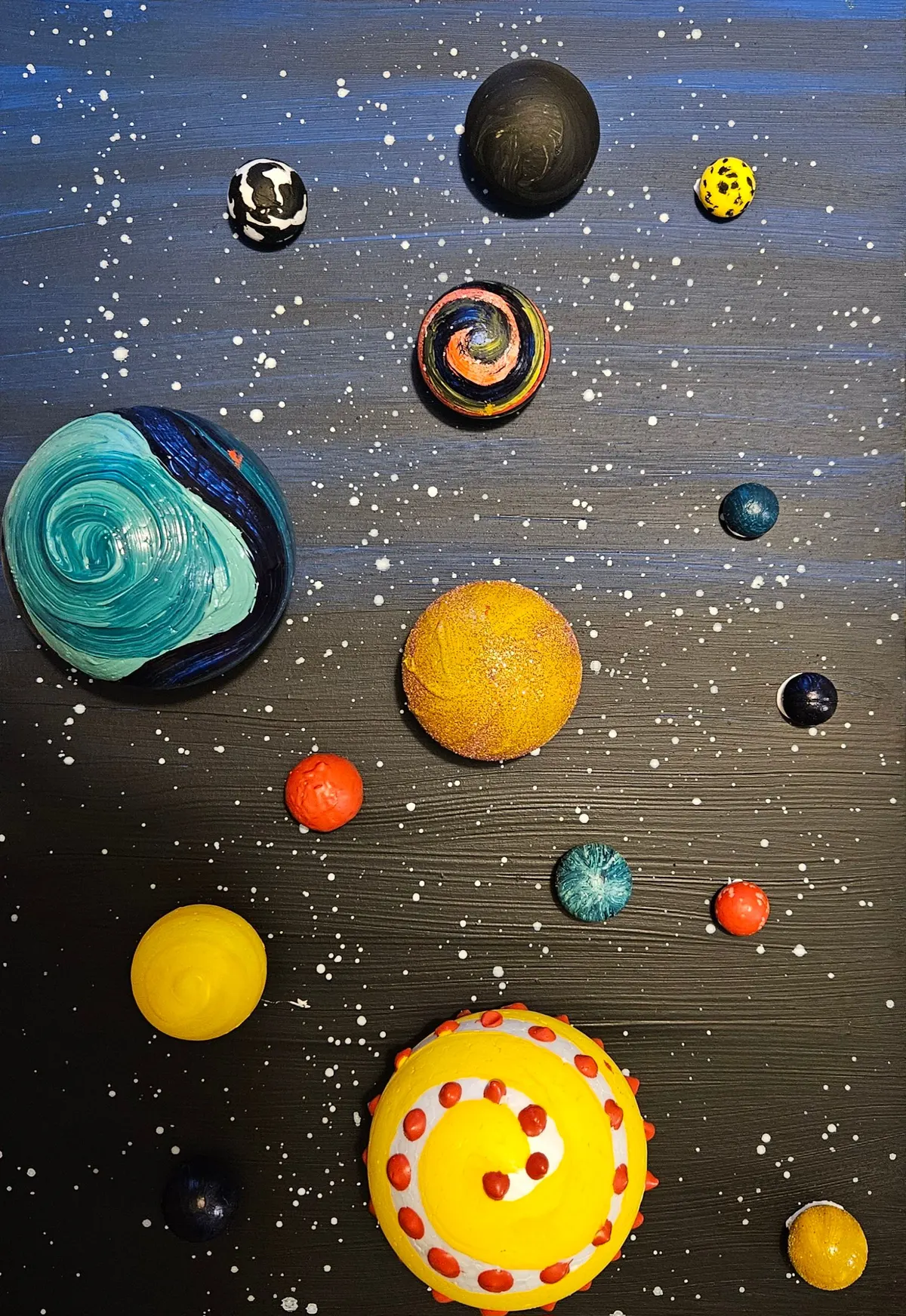 Fifteen hand-painted half-sphere planets, including a yellow sun and a teal swirl, glued on a starry black board