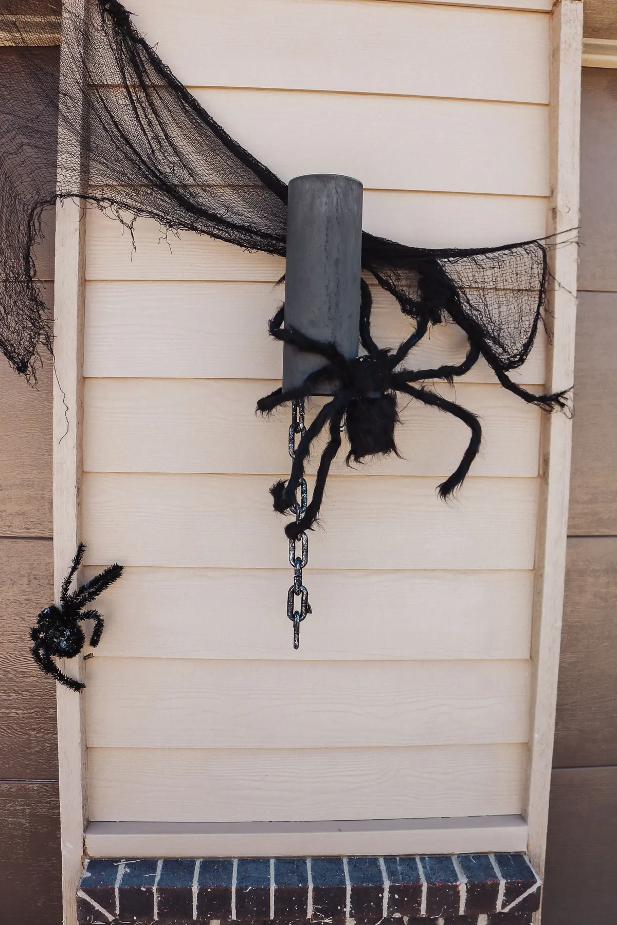 Large black fuzzy spider on a gray wall light with torn black gauze draped