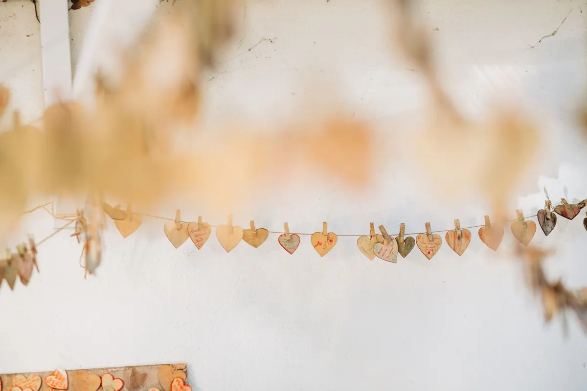 Tan and cream paper hearts hanging from string with small wooden clothespins against a white plaster wall