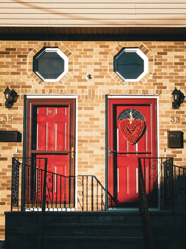 Brick house with two red doors, a red heart-shaped wreath on the right door and two black wall lanterns