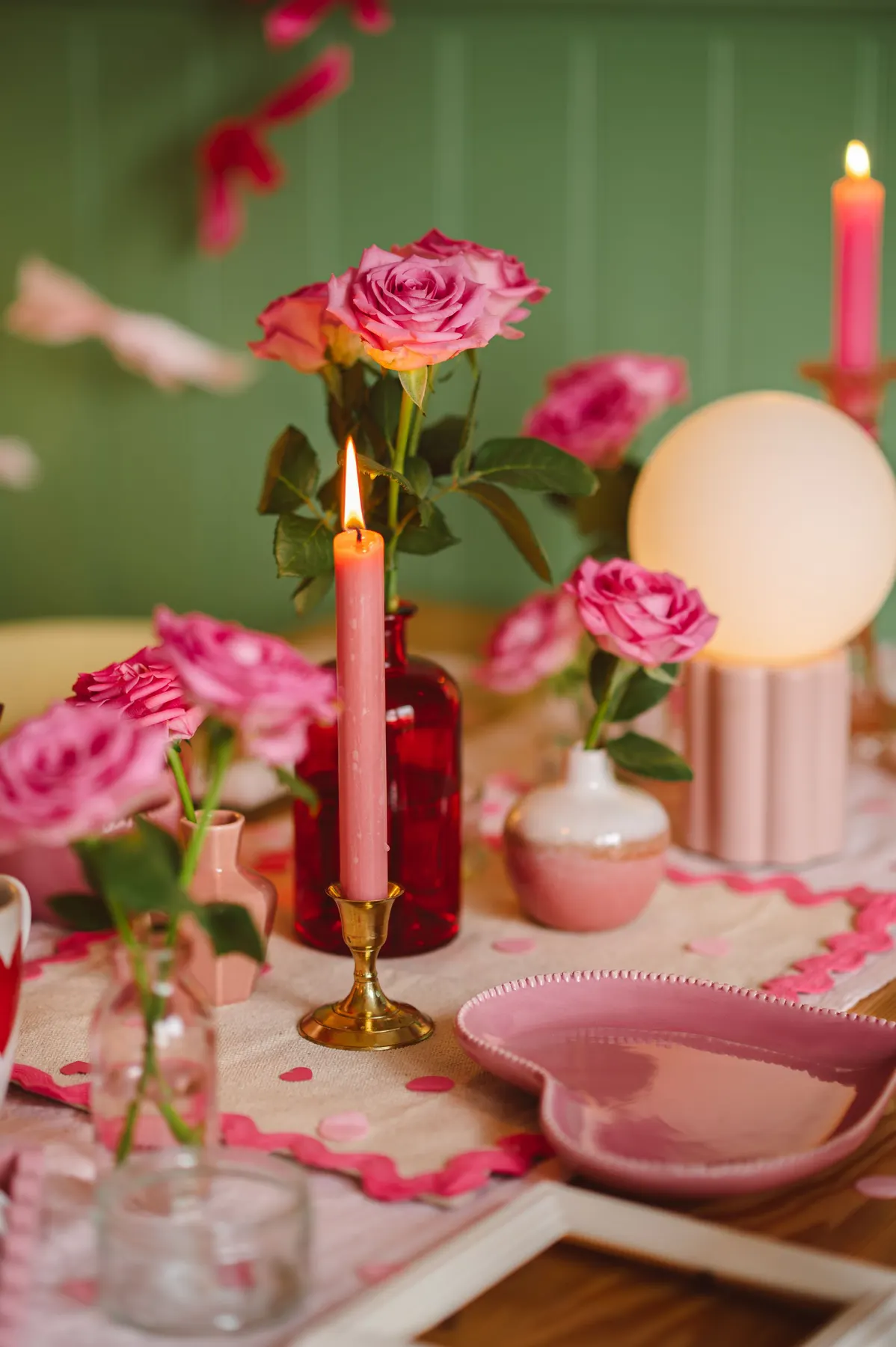 Table with a cream runner, pink confetti, pink roses in small vases, two lit pink tapers and a heart plate