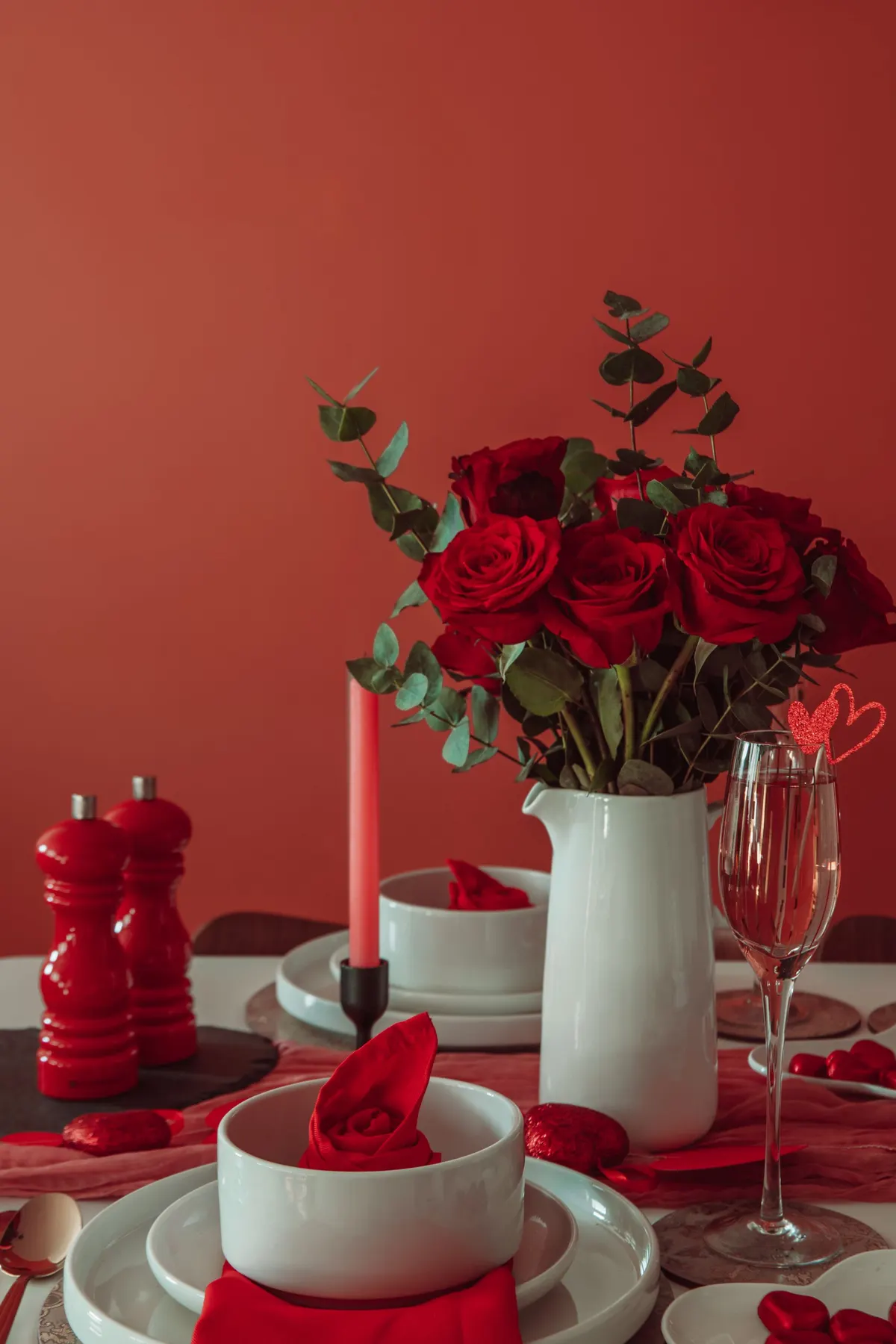 Dinner table with a white pitcher of red roses, white bowls with red napkins and glitter heart decorations