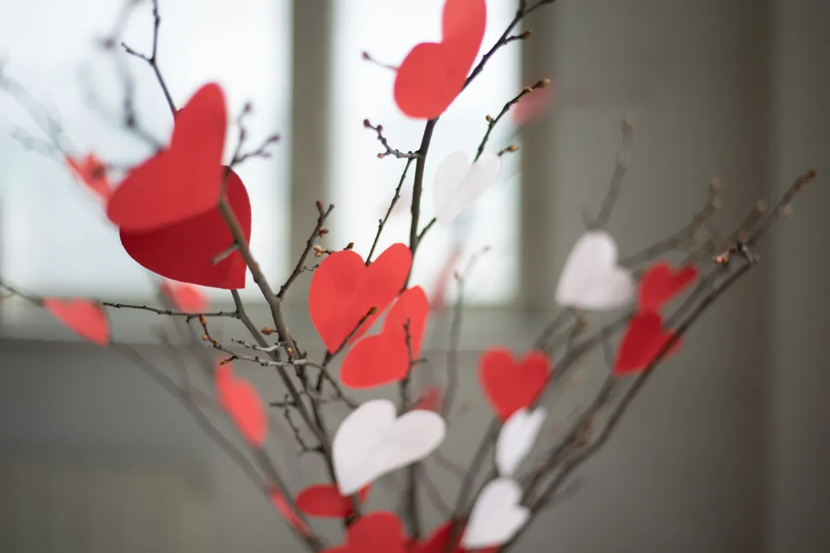 Bare brown twigs hung with red and white paper hearts in front of a bright window