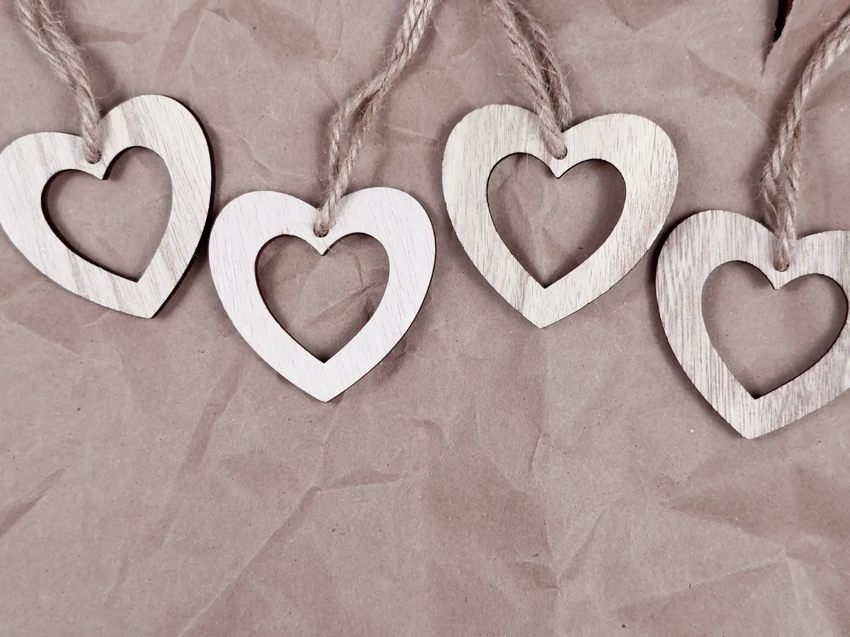 Four whitewashed wooden hearts with open centers tied to beige twine on creased brown kraft paper